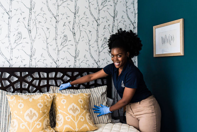 House cleaning specialist smiling and making a bed