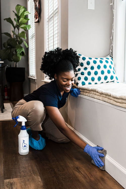 Home Clean Heroes cleaning technician smiling while wiping baseboards in a home