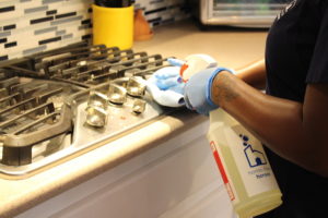 Home Clean Heroes cleaner disinfecting a stove while wearing gloves