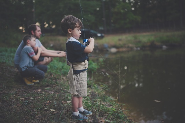 Little boy fishing on a river next to his dad and brother