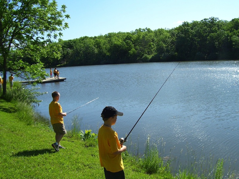 Boys fishing along the side of a lake on a sunny day