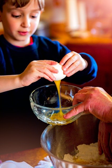 Little boy cracking an egg in a bowl for baking