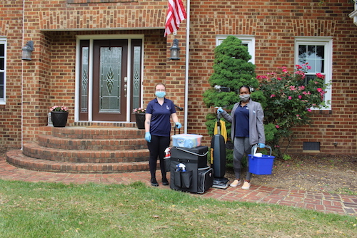 Two women wearing gloves and masks with cleaning equipment in front of customer house