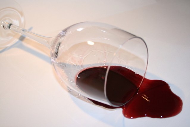 Wine glass tipped over with red wine spilling out onto surface