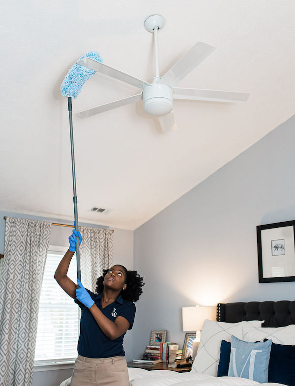 House cleaning company dusting off ceiling fan blades